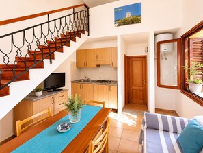 Eine Küche mit Holzschränken, einem Esstisch mit Stühlen, einem Fernseher und einer Treppe mit Geländer.