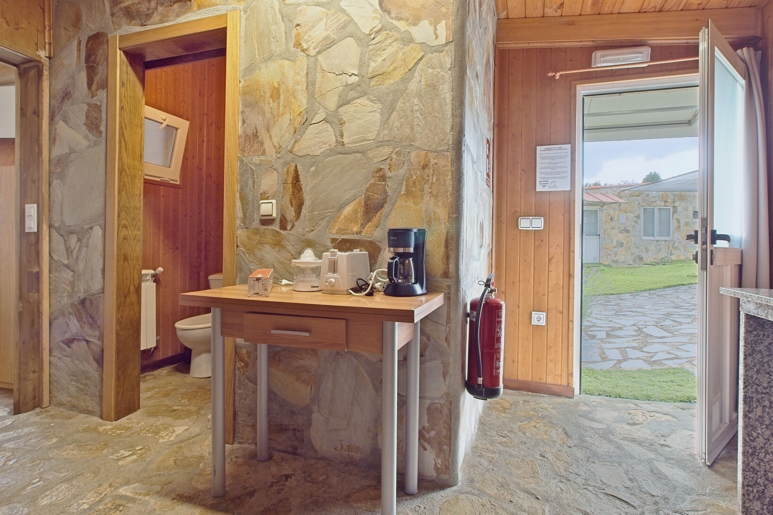 Une salle de bain avec un mur en pierre, une porte en bois et une petite table sur laquelle sont posés des articles de toilette.
