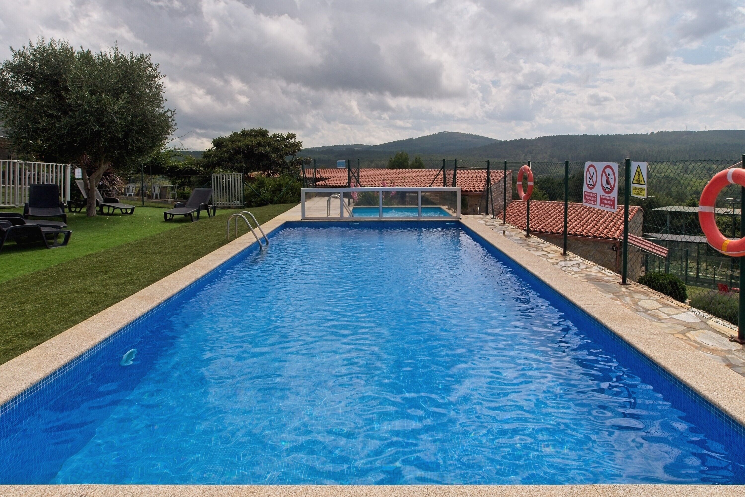Une piscine rectangulaire à l’eau d’un bleu limpide, entourée d’une terrasse carrelée et d’une petite clôture.