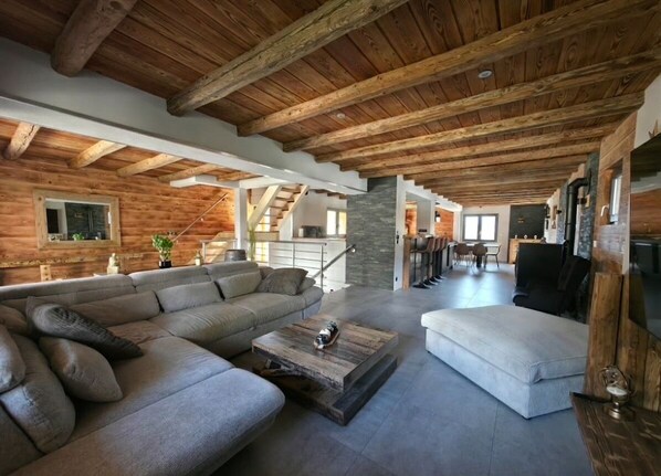 A spacious living area with a wooden ceiling, a large sofa, a coffee table, and a staircase leading to an upper level. - Vrbo Property (Bozel)
