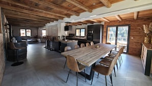 Een ruime woonkamer met houten plafond, een eettafel met stoelen, een keukenhoek en uitzicht op de omgeving.