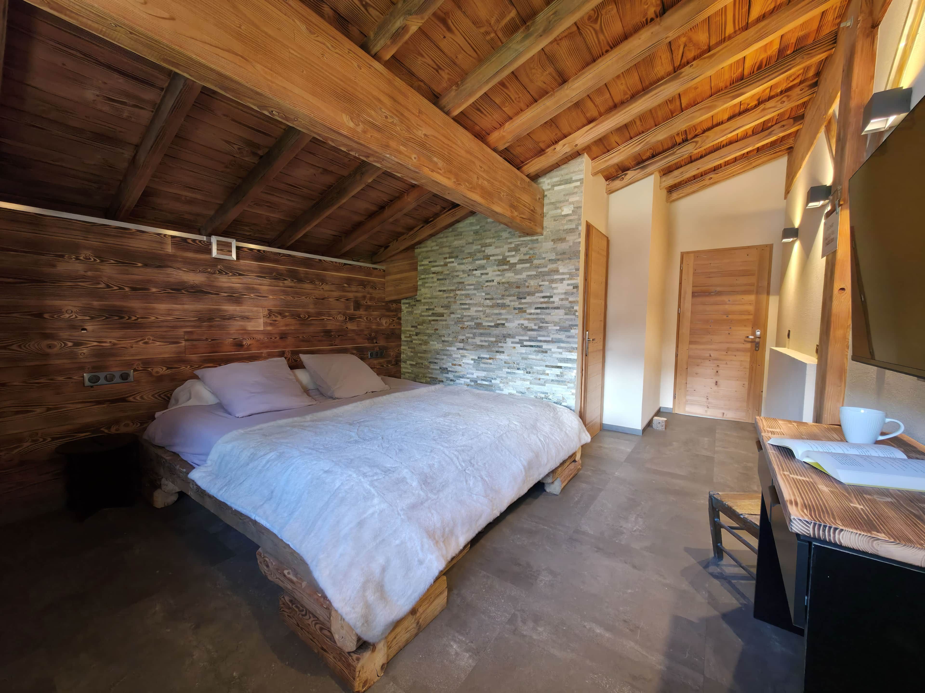 A bedroom with a wooden bed, a stone wall, and a wooden ceiling.