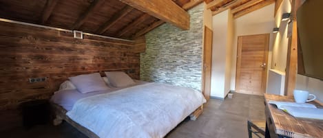 A bedroom with a wooden bed, a stone wall, and a wooden ceiling.