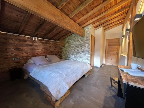 A bedroom with a wooden bed, a stone wall, and a wooden ceiling.