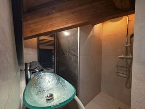 Een badkamer met een glazen wastafel, een douche en een handdoekrek.
