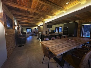 A modern kitchen with a wooden ceiling, a dining area with a large table, and a bar area with stools.
