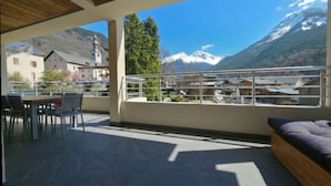 Een balkon met uitzicht op bergen, een eethoek met stoelen en een bed.