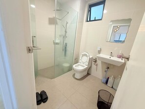 Casa de banho com cabine de chuveiro envidraçada, sanita, lavatório com espelho e janela.