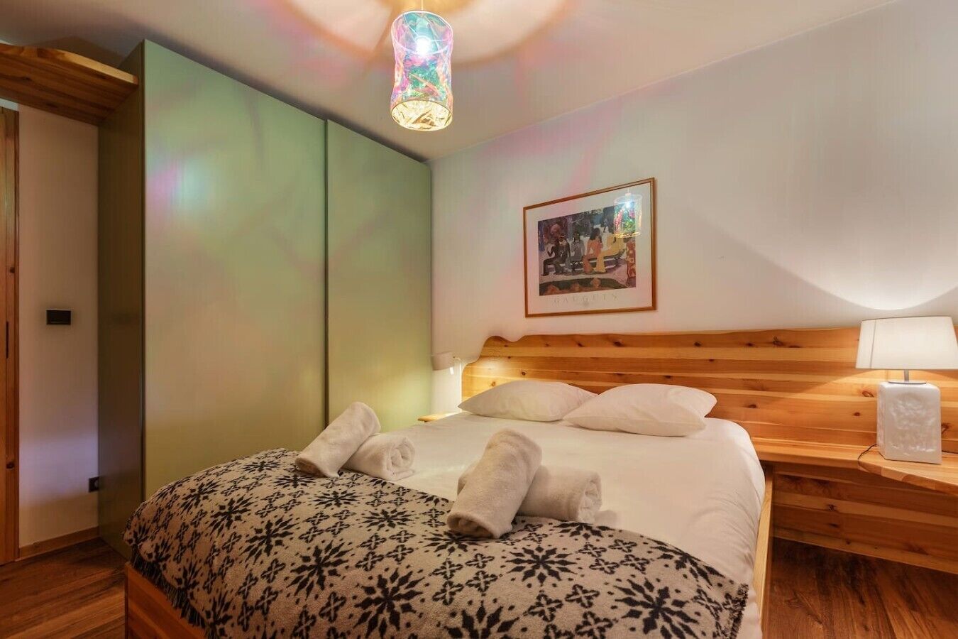 Un dormitorio con cama, mesita de noche, lámpara, un cuadro y una lámpara colgante original.
