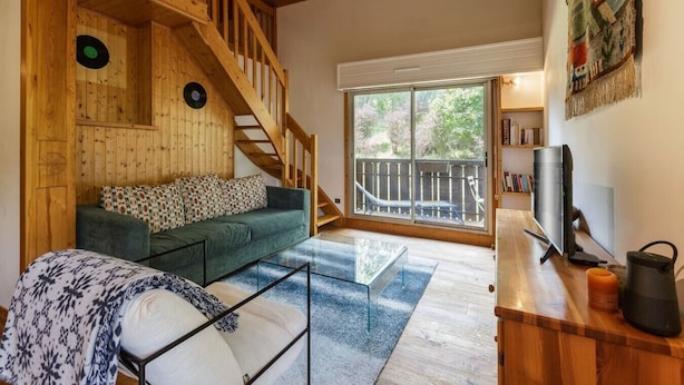 Ein Holzinnenraum mit Treppe, einem grünen Sofa, einem Glastisch und einem Fernseher auf einem Holzständer.