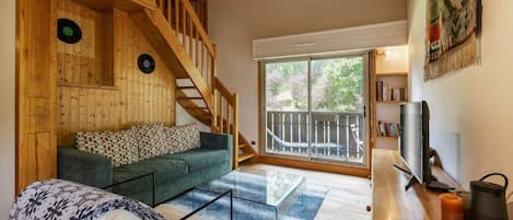 A wooden interior with a staircase, a green sofa, a glass coffee table, and a TV on a wooden stand.