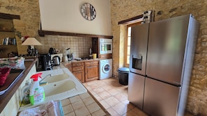 A kitchen with a washing machine, a microwave, a refrigerator, a sink, and a clock on the wall. - Domaine de Rebeyrotte (Pressignac-Vicq)