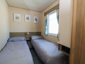 A compact RV bedroom with two beds, a small table, and a window with curtains. - Kensington 49 (Blackpool)