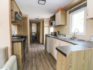A compact kitchen with wooden cabinetry, a microwave, a toaster, and a sink. - Kensington 49 (Blackpool)