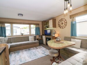 A cozy living area with a sofa, a small round table, a television, and a clock on the wall. - Kensington 49 (Blackpool)