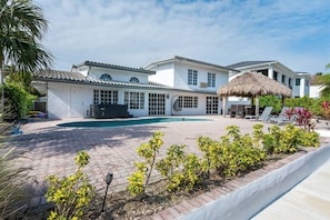Ein zweistöckiges Haus mit Pool, einer überdachten Terrasse und einem Reetdachgebäude.