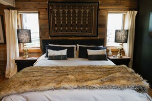 Een slaapkamer in blokhutstijl met een groot bed, twee nachtkastjes met lampen, en een wanddecoratie boven het bed.