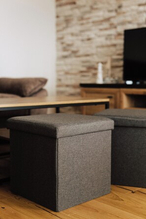 Ein modernes Wohnzimmer mit Holzboden, grauem Sofa, Couchtisch aus Holz und Fernseher auf einer Holzkommode.