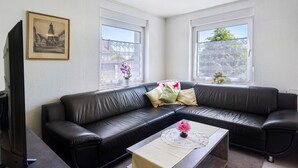 Un salón con un sofá de cuero negro, una mesa de centro con un florero y un cuadro en la pared.