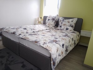 Ein Bett mit floralem Überwurf, ein Nachttisch mit Lampe und eine kleine Schublade.