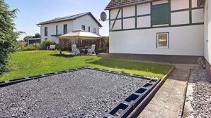 Un barrio residencial con un camino de grava, un patio con mobiliario exterior y una casa tradicional con tejado de baldosas.