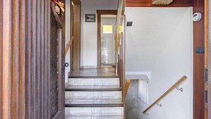 Una escalera de madera con barandilla, una puerta con panel decorativo y un perchero de pared.