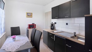 Cocina compacta con armarios negros, microondas, lavamanos y una mesa de comedor con sillas.