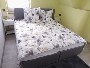 Ein Bett mit floralem Bettzeug, ein Nachttisch mit Lampe und ein Beistelltisch.