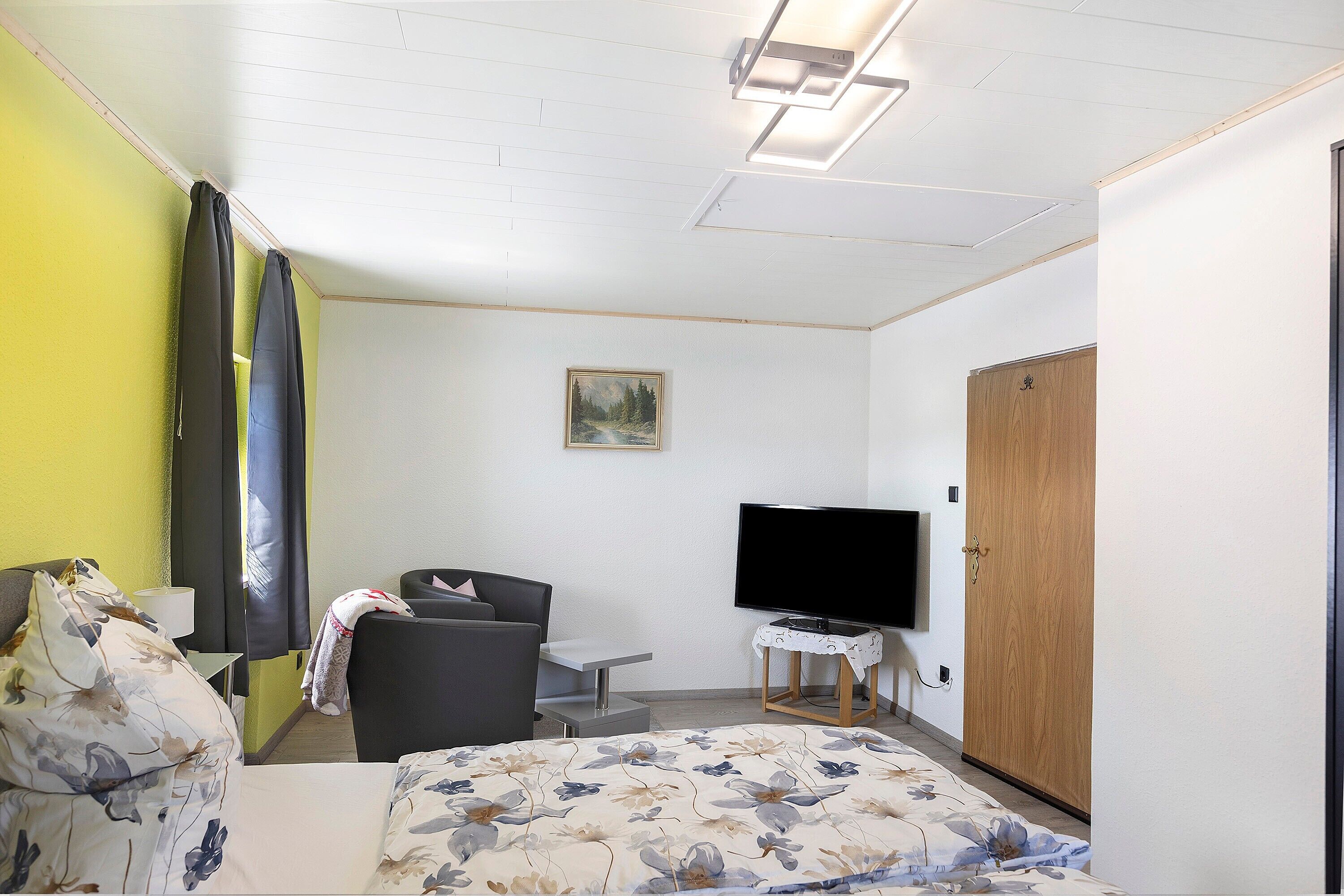 Ein Hotelzimmer mit Bett, Sessel, Fernseher, Schreibtisch und Kleiderschrank.