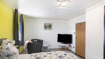 Ein Hotelzimmer mit Bett, Sessel, Fernseher, Schreibtisch und Kleiderschrank.