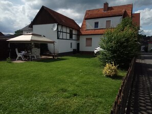 Ein Haus mit weißer Fassade und rotem Dach, einer Satellitenschüssel und einer überdachten Terrasse mit Stühlen.