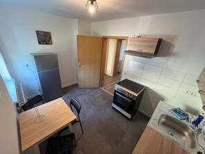 A compact kitchen with a refrigerator, stove, sink, and a dining area with chairs. - Cozy fitters apartment at the Geiseltal lake (Braunsbedra)