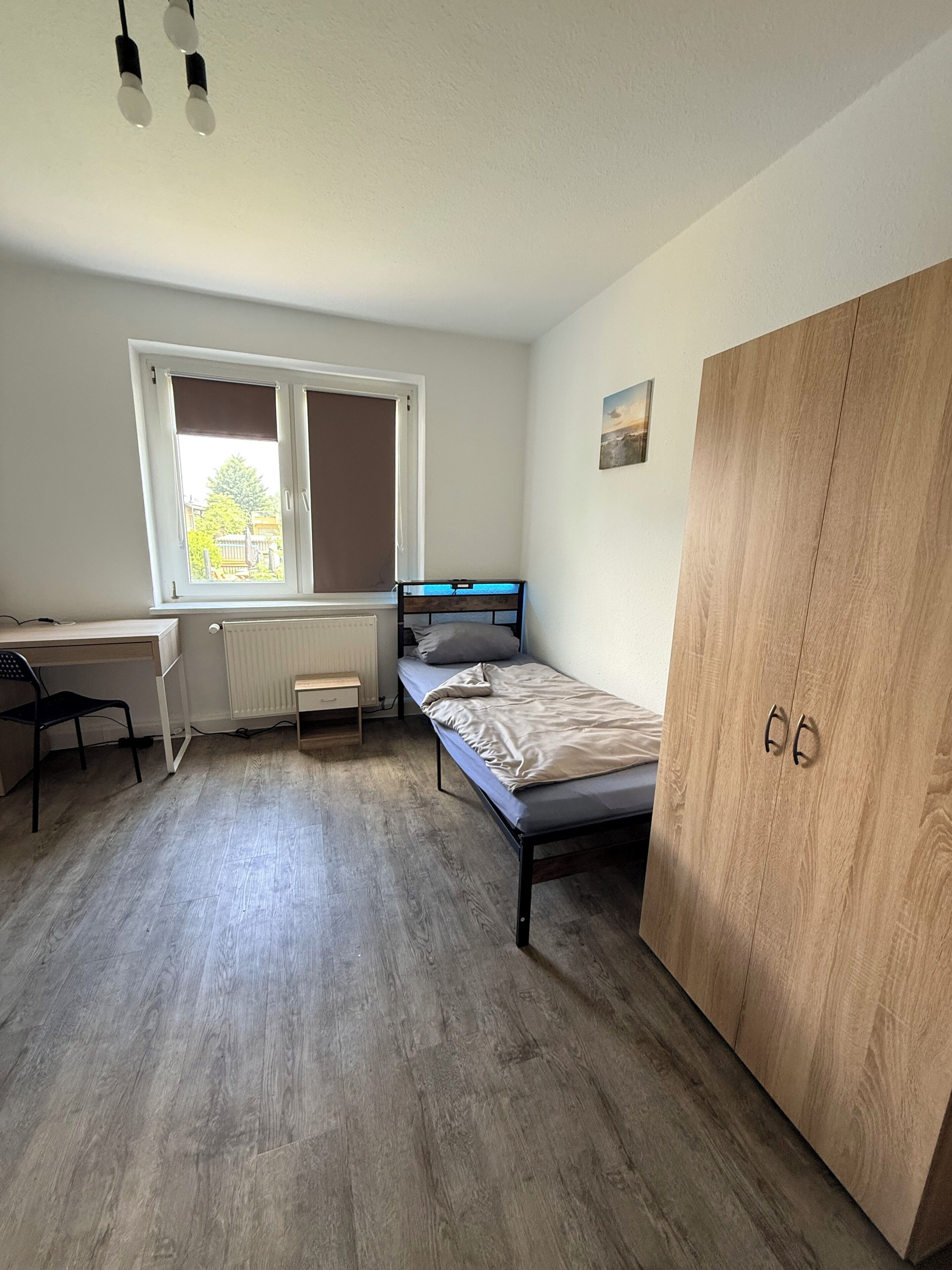 Ein Schlafzimmer mit Bett, Schreibtisch, Heizkörper, Fenster und Kleiderschrank.