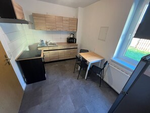 Eine kleine Küche mit Spüle, Herd und Mikrowelle, ein Esstisch mit Stühlen und ein Fenster mit Blick auf Grünflächen.