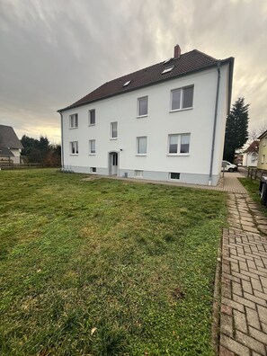Ein weißes, zweistöckiges Gebäude mit einem Ziegeldach, mehreren Fenstern und einem gepflasterten Auffahrt.