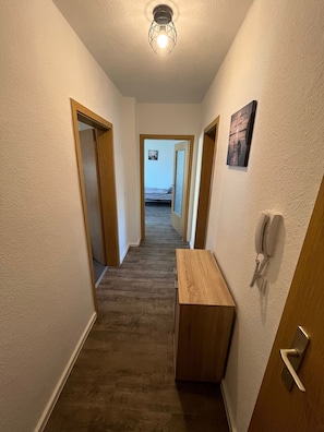 A hallway with wooden doors, a wooden bench, a wall-mounted telephone, and a ceiling light fixture. - Cozy fitters apartment at the Geiseltal lake (Braunsbedra)