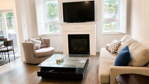 Ein Wohnzimmer mit Kamin, Flachbildfernseher, Glastisch und einer Couch.