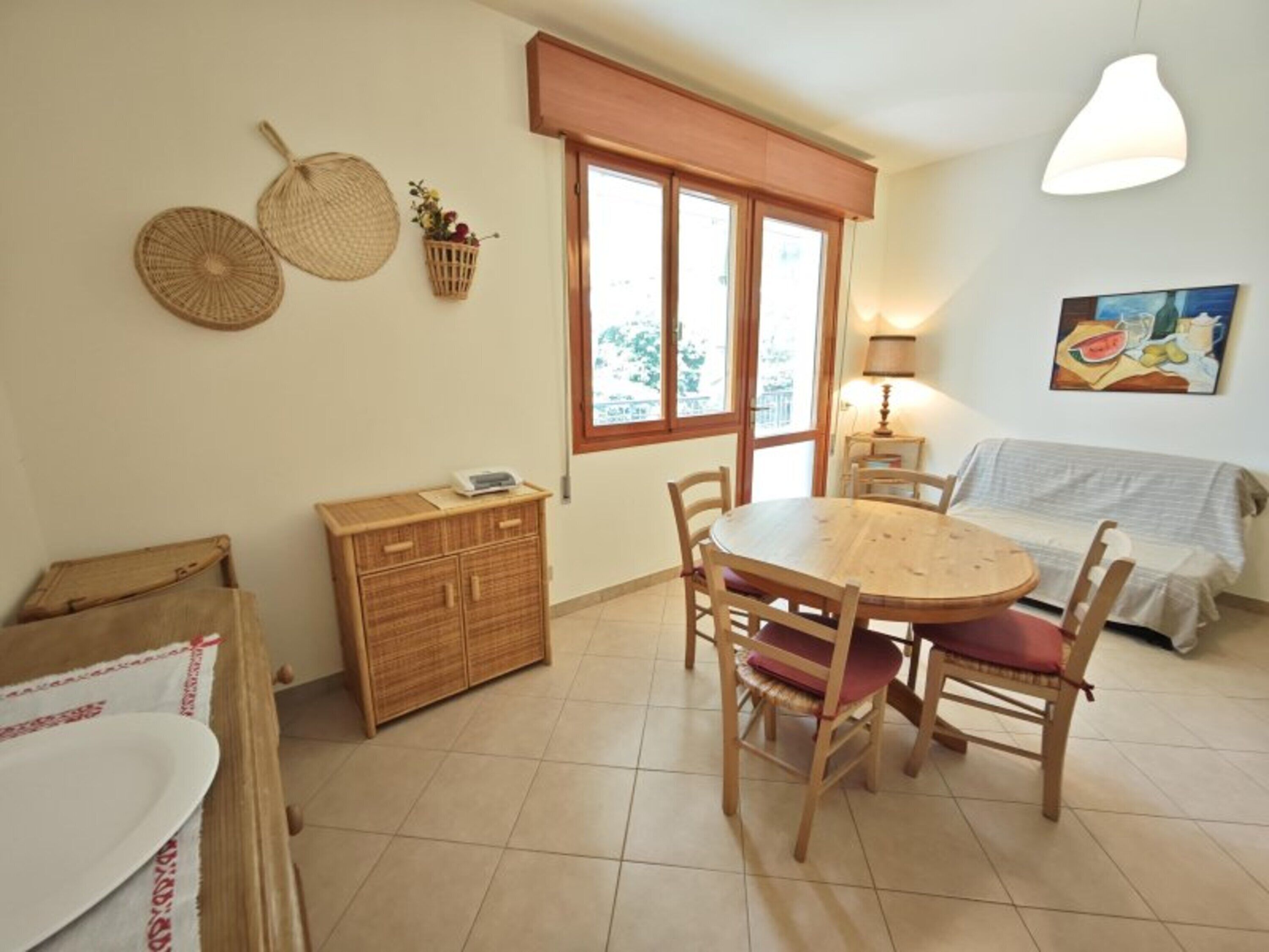 Ein Essbereich mit einem runden Holztisch, Stühlen, einem Schrank, einem Fenster mit Jalousien, einer Lampe und einem Bild an der Wand.