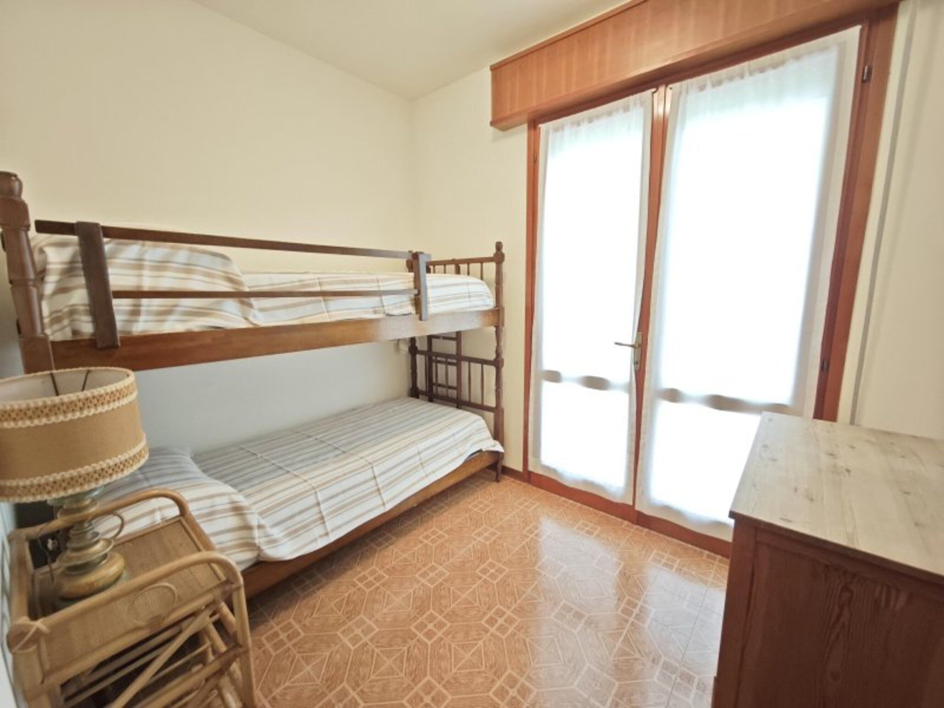 A room with a bunk bed, a small table with a lamp, a cabinet, and a sliding glass door to the outside.