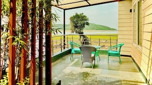 Un balcone con vista su un fiume e delle colline, con poltrone verdi e un tavolo.
