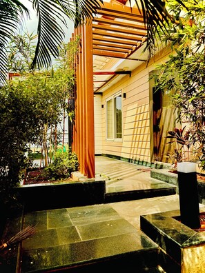 A modern building with a wooden pergola, a concrete pathway, and lush greenery.
