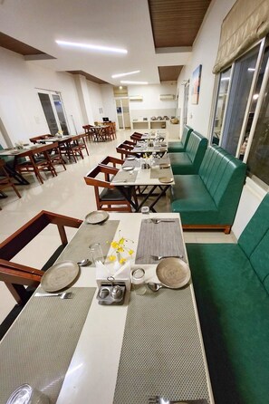 A dining area with multiple tables and chairs, a green sofa, and a kitchen area in the background.