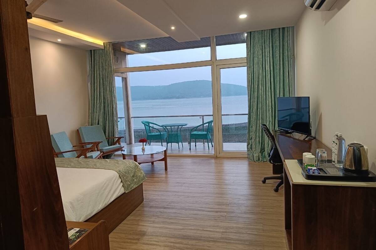 A hotel room with a bed, a desk, a TV, and a balcony with chairs and a table.