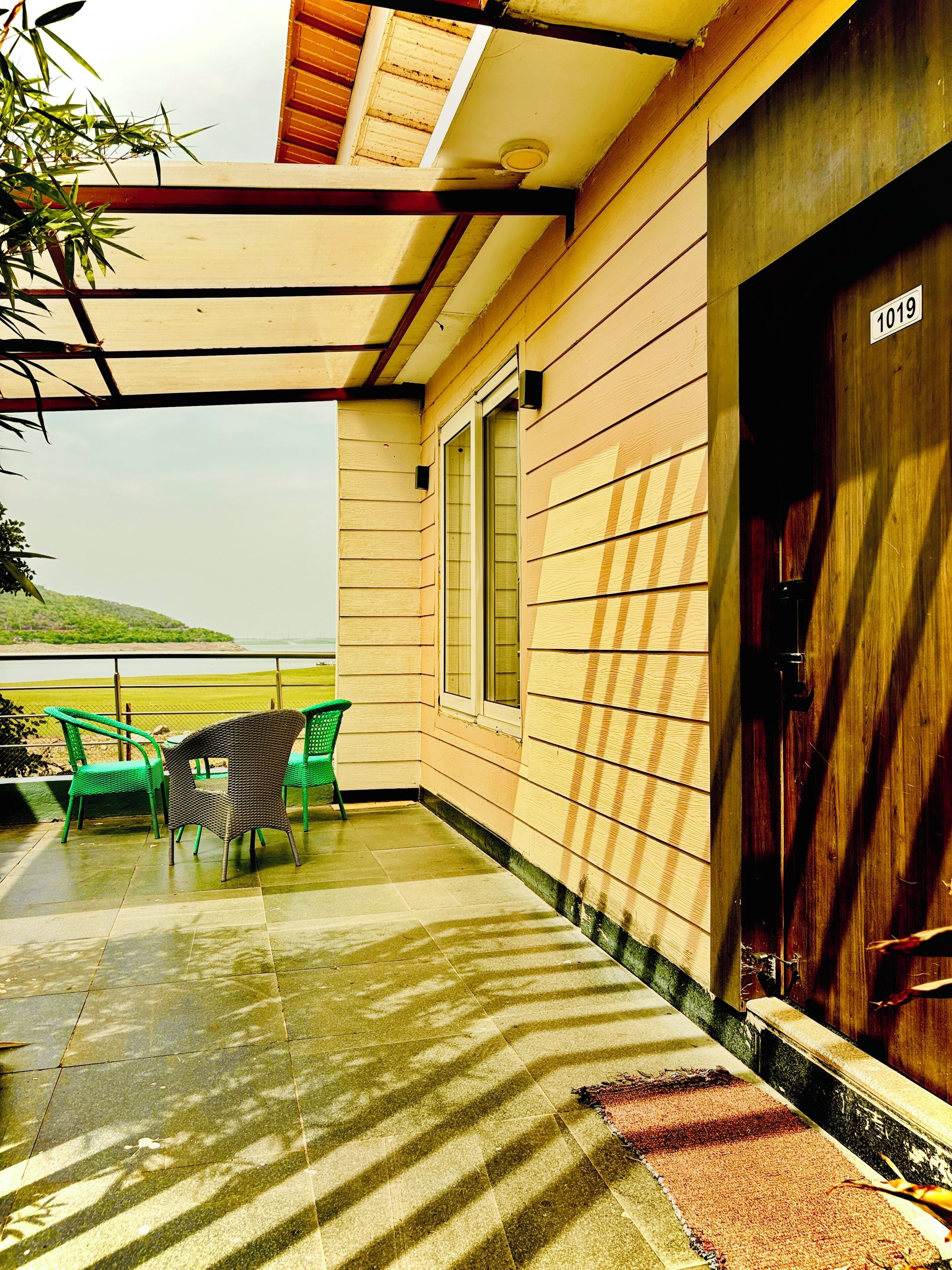 A covered outdoor area with a wooden door marked '1019,' a window, and a green chair.