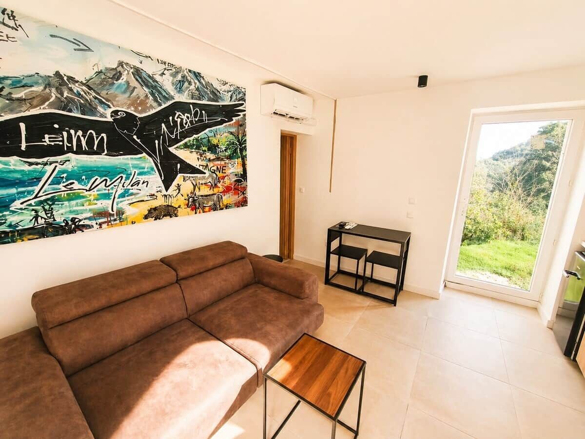 Ein modernes Wohnzimmer mit einem braunen Sofa, einem Holztisch, einem Bild an der Wand und Blick durch eine Glastür.