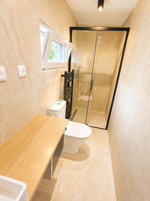 Een moderne badkamer met een houten wastafelmeubel, een wit toilet, een douchecabine van glas en een raam voor natuurlijk licht.