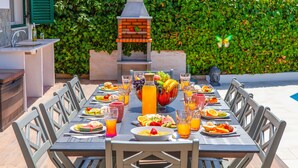 An outdoor dining area with a long table set for a meal, surrounded by chairs, and a grill in the background. - Elegant Villa w/ Heatable Pool and BBQ (Albufeira)