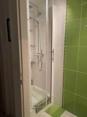 Une douche fermée par des parois en verre, dotée d’un pommeau de douche à main et d’un robinet mural.