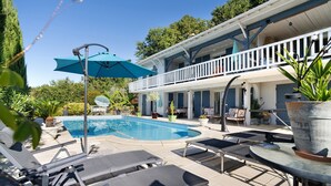 A poolside area with lounge chairs, a pool, and a building with a balcony.