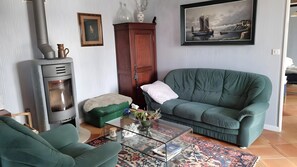 Una sala de estar con sofá, sillón, mesa de centro de vidrio, chimenea, armario y un cuadro en la pared.
